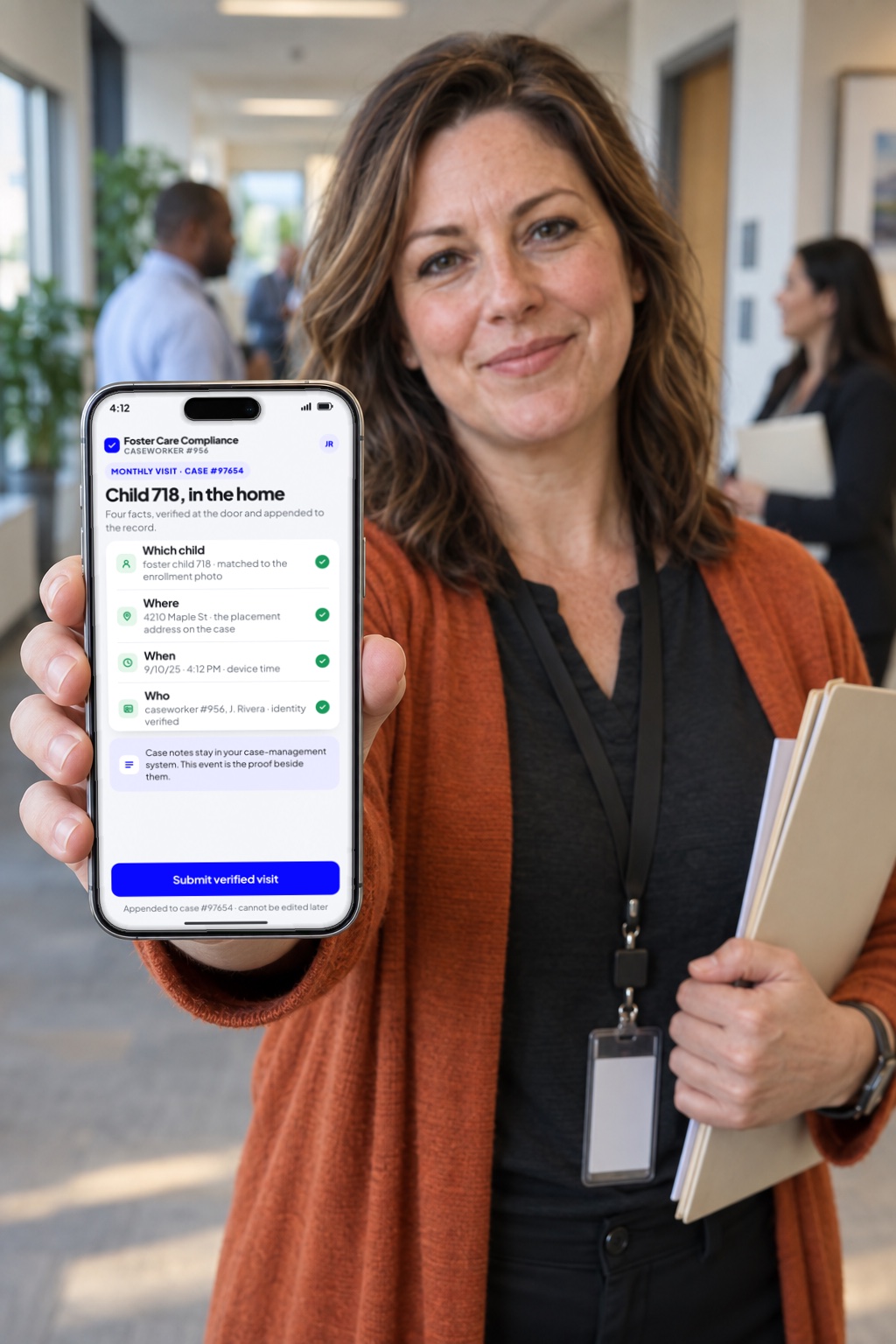 A caseworker in a county-office hallway holds up her phone showing a verified monthly visit